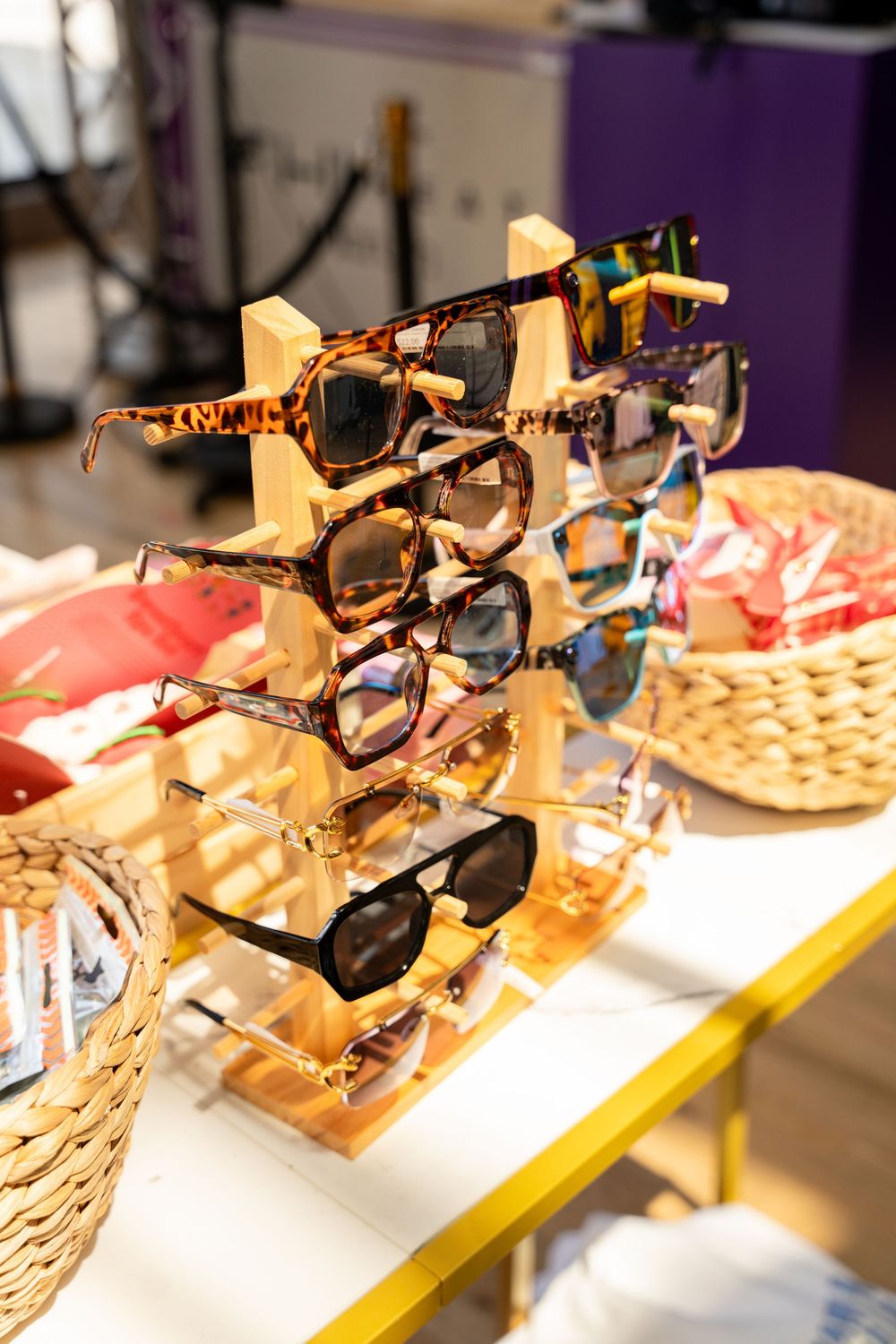 Wooden display stand with multiple stylish tortoiseshell and black sunglasses on a white table in a retail store.