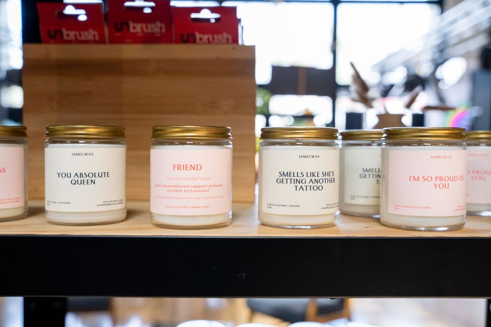 Humorous scented candles with funny labels on a wooden shelf in a boutique gift shop.