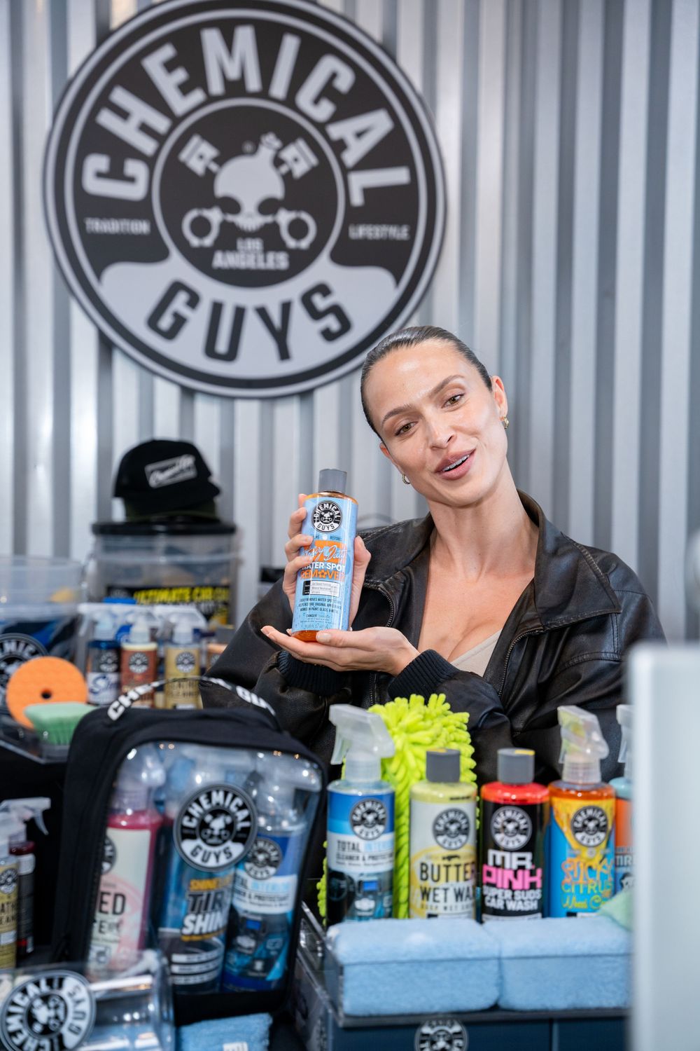 Woman holding Chemical Guys car care product at a branded display booth with detailing supplies.