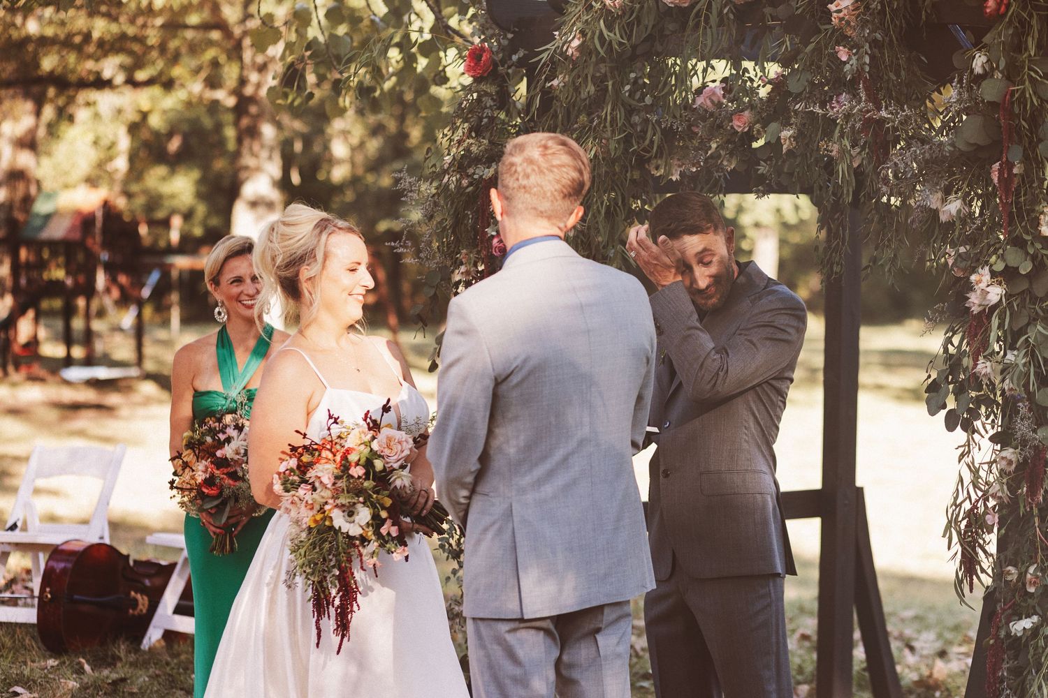 Man in blue shirt and tan suit holds decorative wire flowers at a wedding celebration.