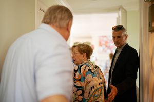 Three adults engaged in conversation near a doorway inside a bright, warmly lit home.