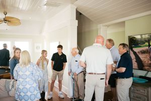 Group of people gathered indoors in a bright coastal home, engaged in conversation during a social gathering.