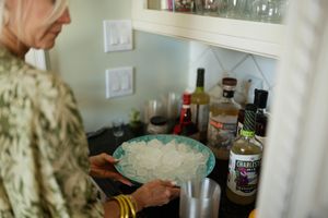 Woman holding a teal bowl of ice near a home bar with wine bottles and cocktail mixers.