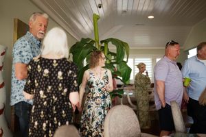 Group of adults socializing indoors at a casual gathering near a large tropical plant in a bright room.