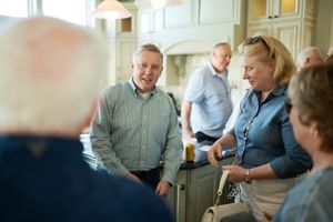 Group of adults socializing indoors, smiling and engaging in conversation at a casual gathering.