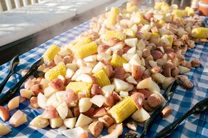 A colorful seafood boil spread with corn, red potatoes, sausage, and shrimp on a blue checkered tablecloth.