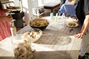 Outdoor wooden table with bowls of food, plates, and condiments during a casual gathering.