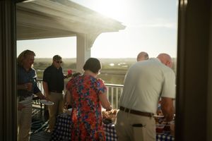 Group of adults socializing around a buffet table on a sunlit outdoor deck at sunset.
