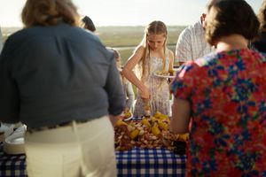 Young girl serving herself food at an outdoor seafood buffet table surrounded by adults.