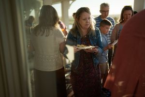 Woman holding a plate of food at a casual outdoor gathering with family and friends in warm evening light.
