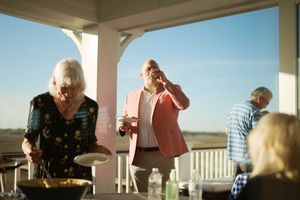 Elderly friends gather on a sunny porch for an outdoor party, sharing food and conversation on a bright day.
