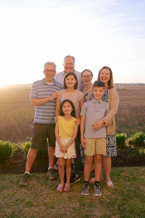 Family of seven smiling together outdoors at golden hour with a scenic marsh field in the background.