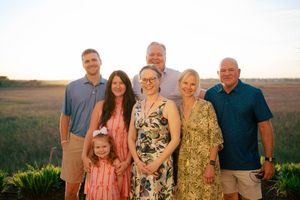 Family group of seven posing outdoors at sunset in a golden field, smiling together for a portrait.