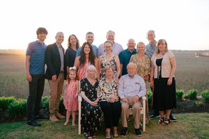 Large multigenerational family group portrait outdoors at sunset, with elderly couple seated in front row.