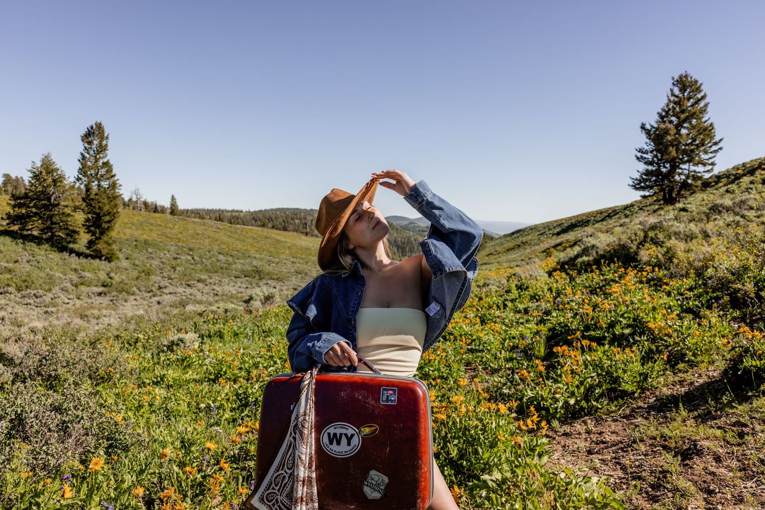 Woman drinking from a bottle in a wildflower meadow, wearing a hat, with a red phone case featuring a WY sticker.