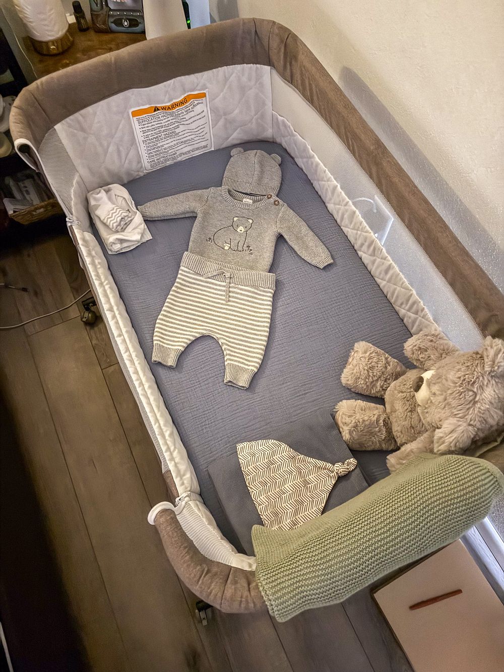 A neatly arranged bassinet with neutral baby clothes and stuffed animals ready for newborn.