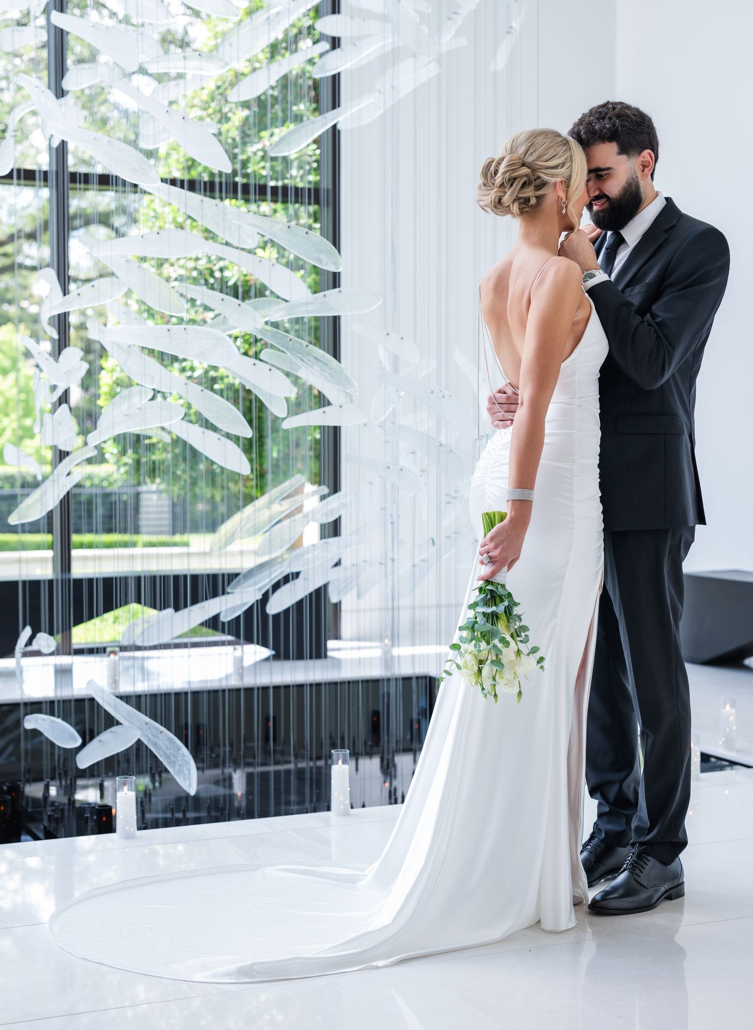 Bride in white gown and groom in black tuxedo share an intimate moment in a modern venue with elegant decor.