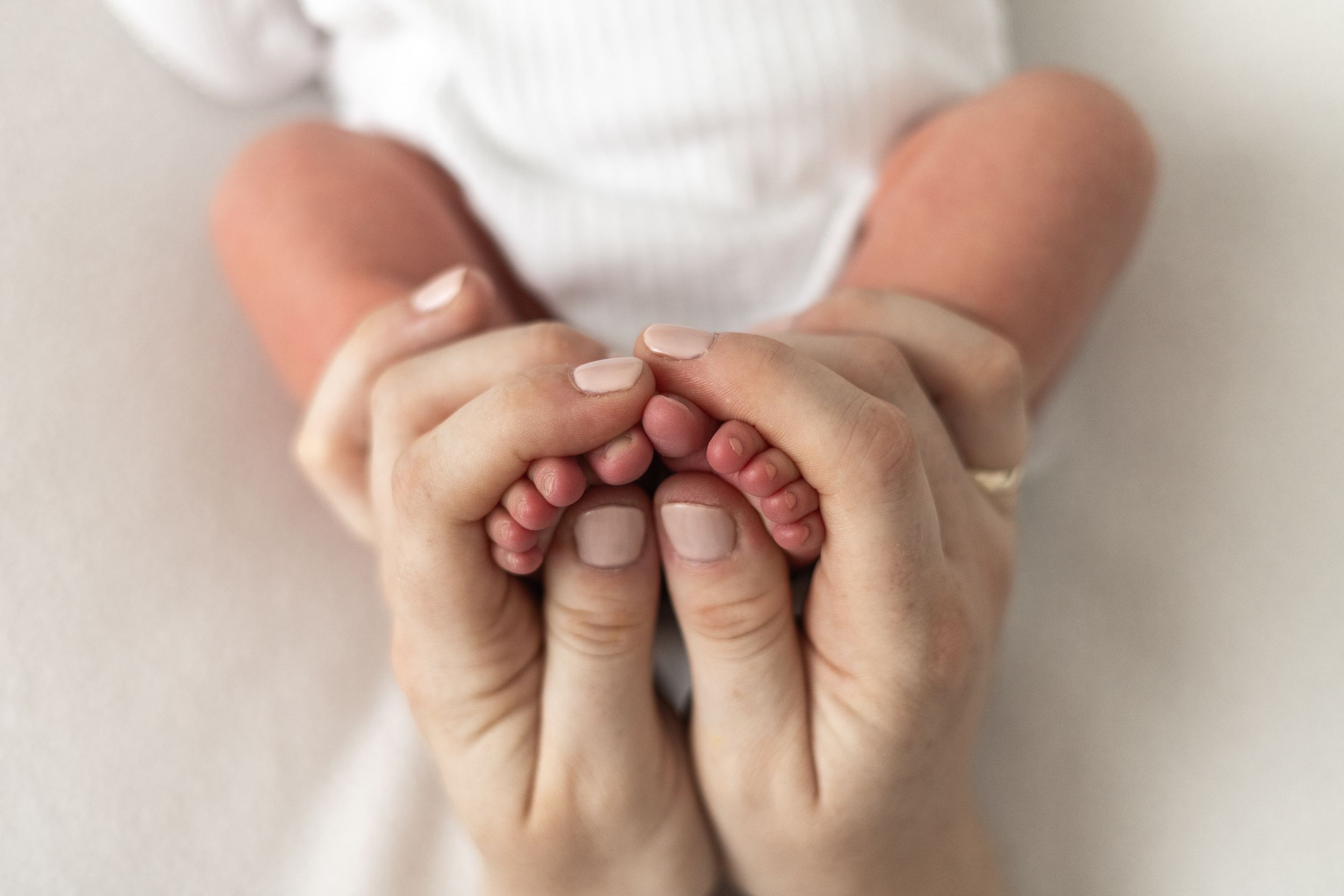 Mum and Dads hands gently cradling tiny newborn baby feet, during newborn photographer Nottingham
