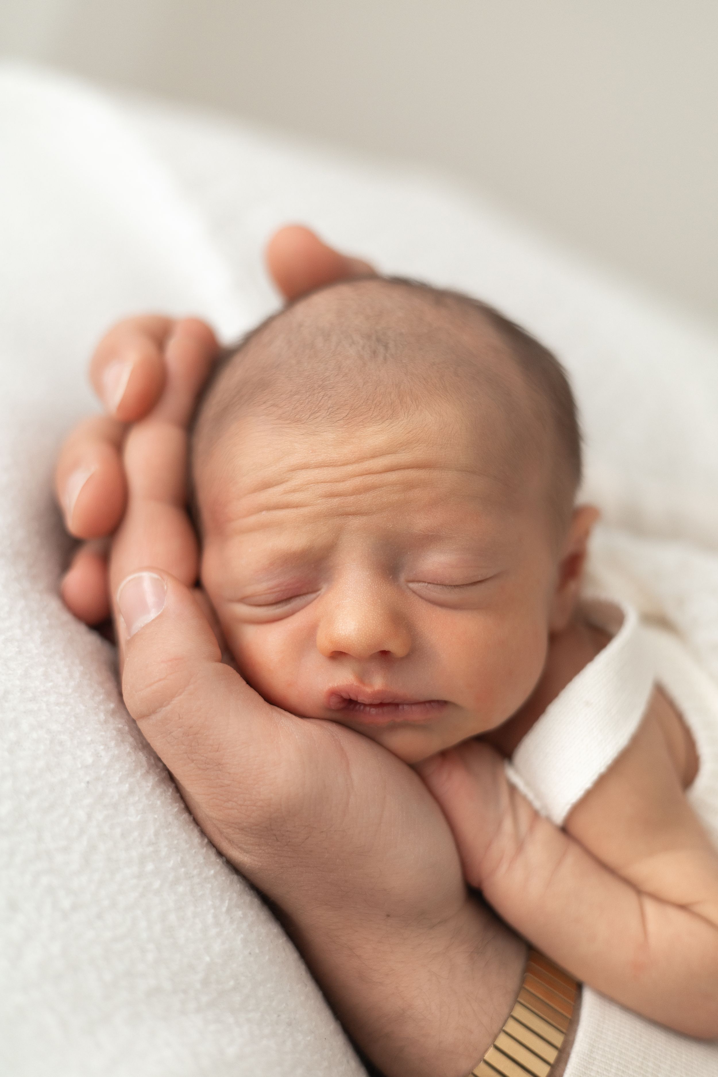 Newborn baby sleeping peacefully cradled in an dads hands on a soft white blanket during newborn photographer Nottingham