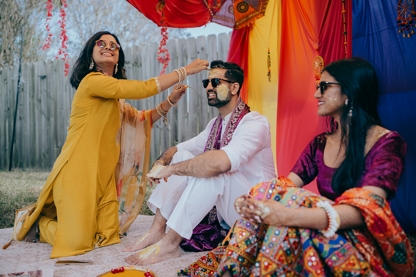 Indian wedding Haldi ceremony with woman in yellow applying turmeric to groom in white sherwani outdoors.