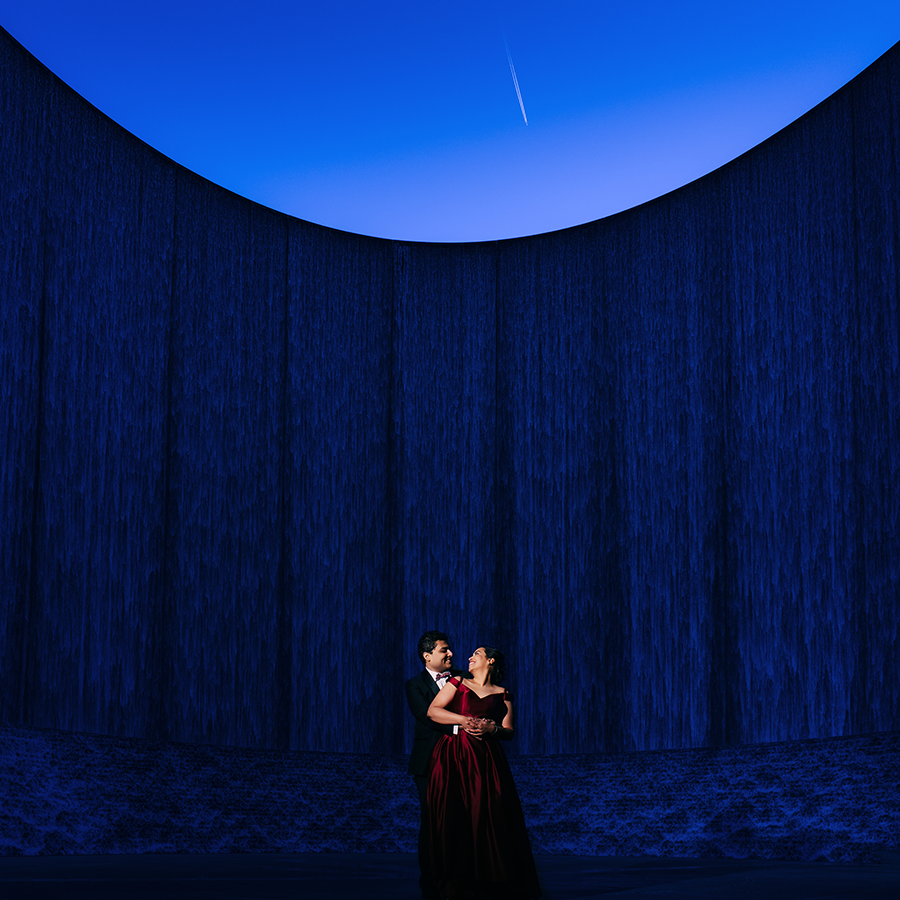 Two opera performers in dramatic blue stage lighting stand beneath a circular opening revealing a starry night sky.