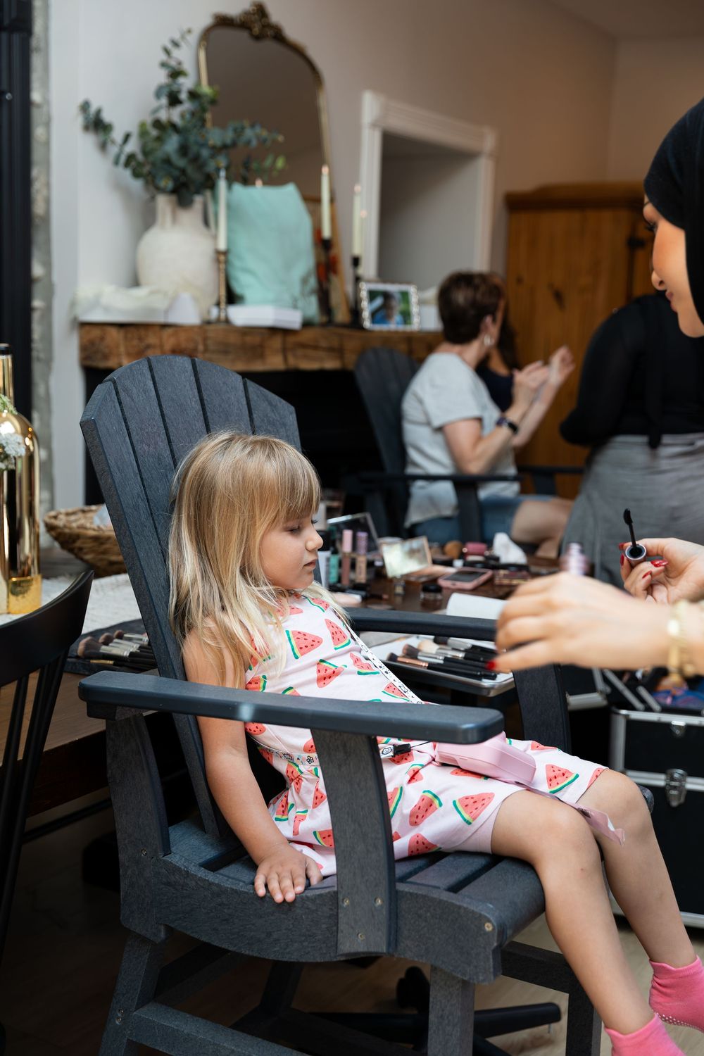 Young girl in a dress sitting in a chair during makeup session with beauty products nearby on the morning of a wedding in Guelph, Ontario