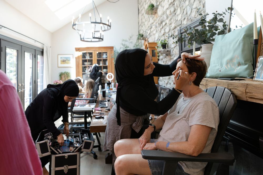 Makeup artist applies makeup to a woman in a bright kitchen during the morning of a wedding in Guelph, Ontario.