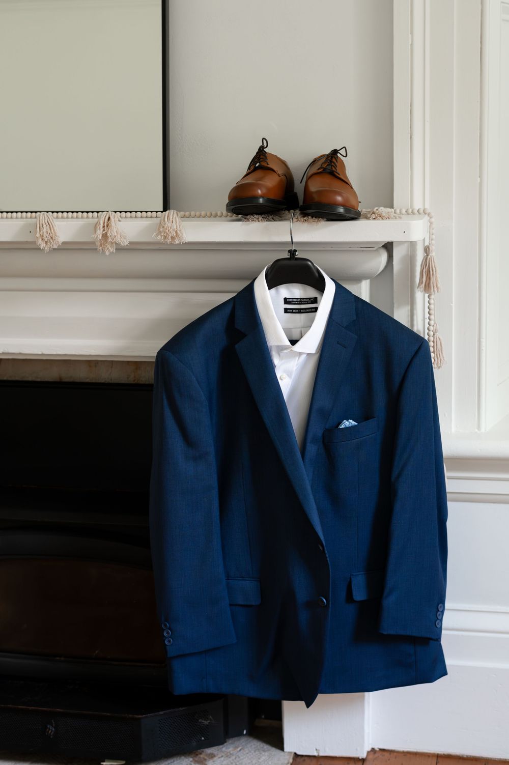 Navy blue suit jacket on hanger with white shirt, brown leather dress shoes on white mantle above fireplace in Guelph, Ontario.