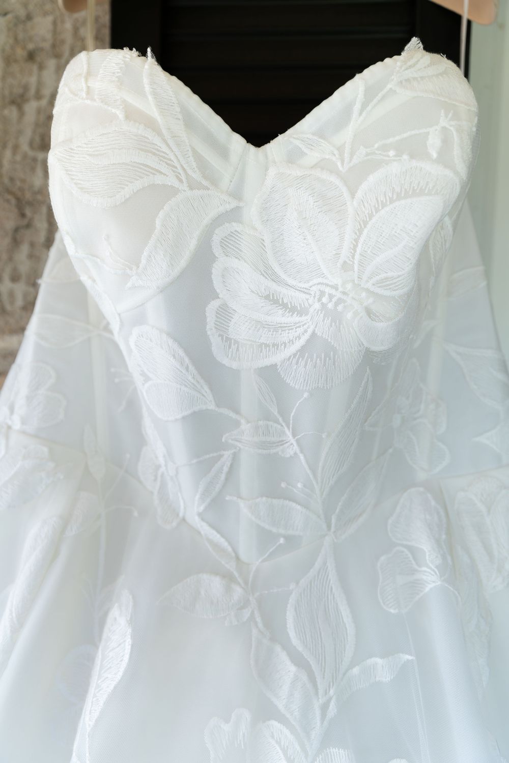 White strapless wedding dress with intricate floral lace embroidery displayed on a hanger on the morning of a wedding in Guelph, Ontario.