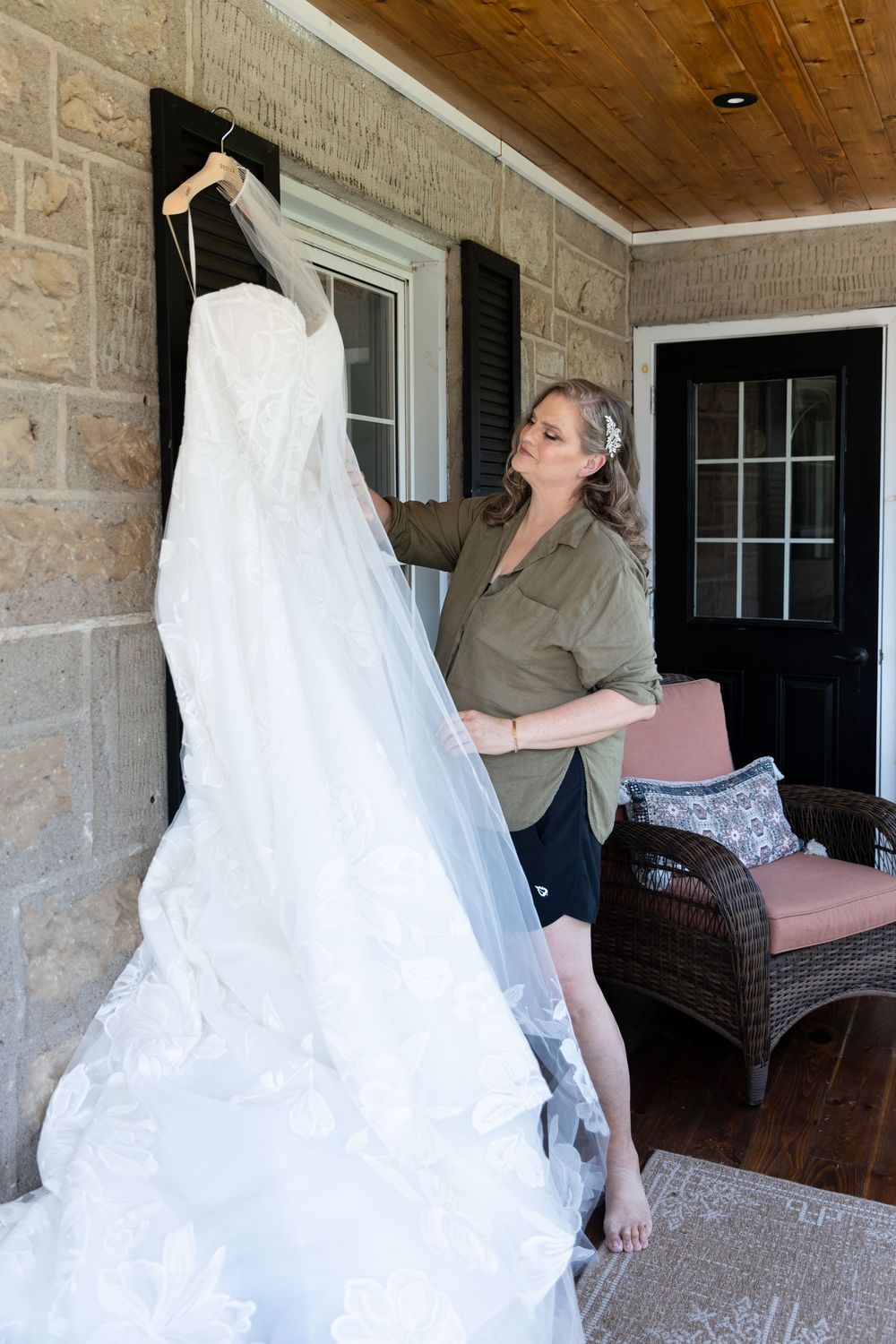 Bride admiring her white lace wedding dress hanging on a porch of a stone house on the morning of her wedding in Guelph, Ontario.