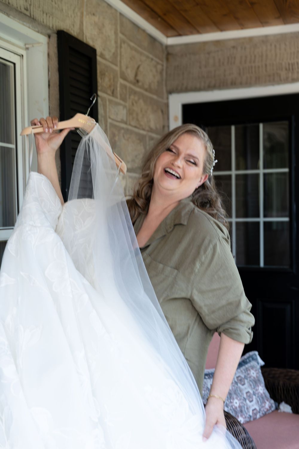 Bride laughing while holding her wedding dress outside on the balcony of her air bnb on the morning of her wedding in Guelph, Ontario.