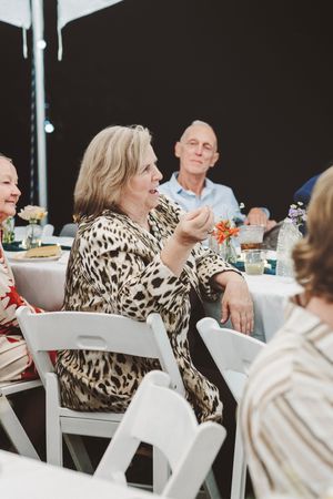 Older woman in leopard print dress conversing at an elegant outdoor dinner party event.