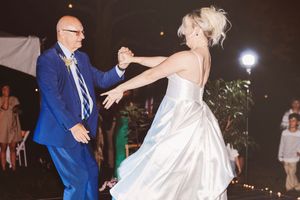 Bride and groom share a romantic first dance at an outdoor wedding reception, with the bride in a white gown.