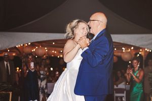 Bride and father share emotional first dance under string lights at outdoor wedding reception tent at night.