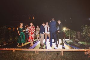 Guests dancing on illuminated dance floor at outdoor evening wedding reception surrounded by string lights.