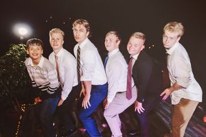 Six young men in dress shirts and ties pose together smiling at an outdoor evening wedding reception.