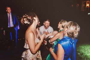 Group of elegantly dressed guests dancing and laughing at a nighttime wedding reception outdoor party.