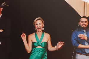 Woman in green halter dress dancing joyfully at a formal event with guests in background.