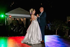 Bride and groom share their first dance on an outdoor dance floor illuminated by colorful lights at a night wedding reception.