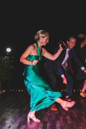 Woman in green satin gown dancing energetically at an outdoor evening wedding reception.