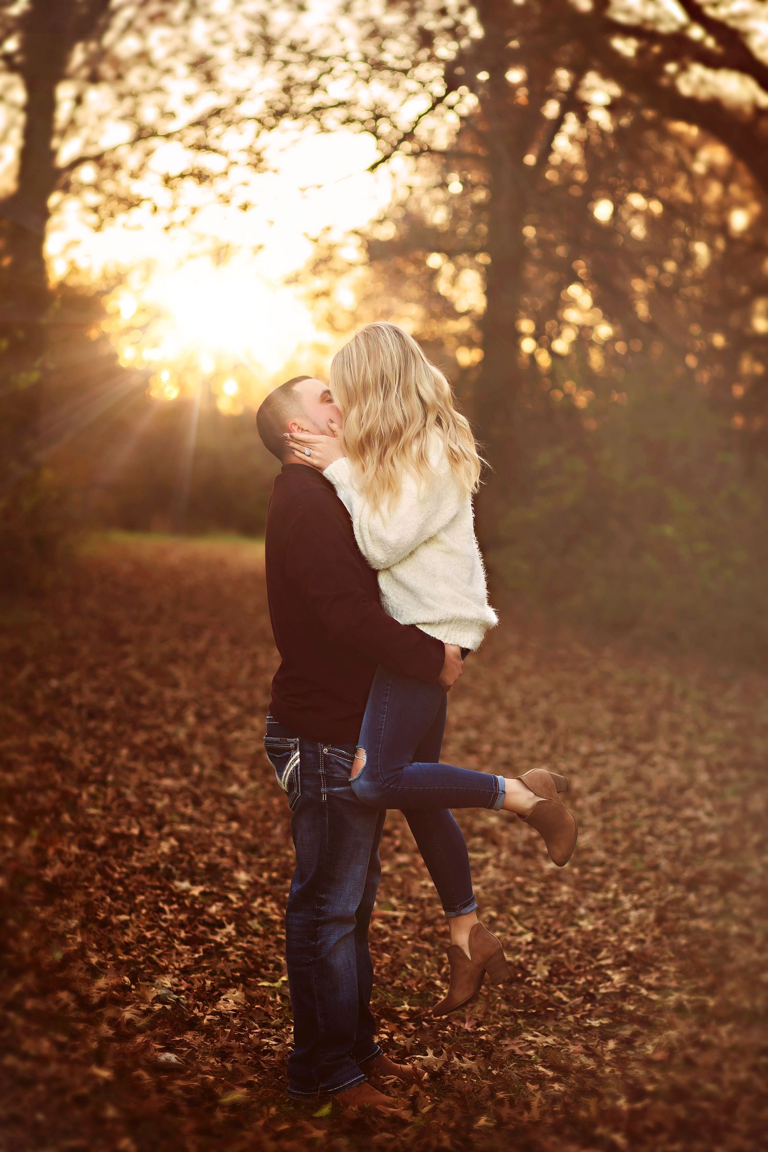 A couple shares a romantic kiss outdoors in warm golden autumn sunlight, surrounded by glowing fall foliage.