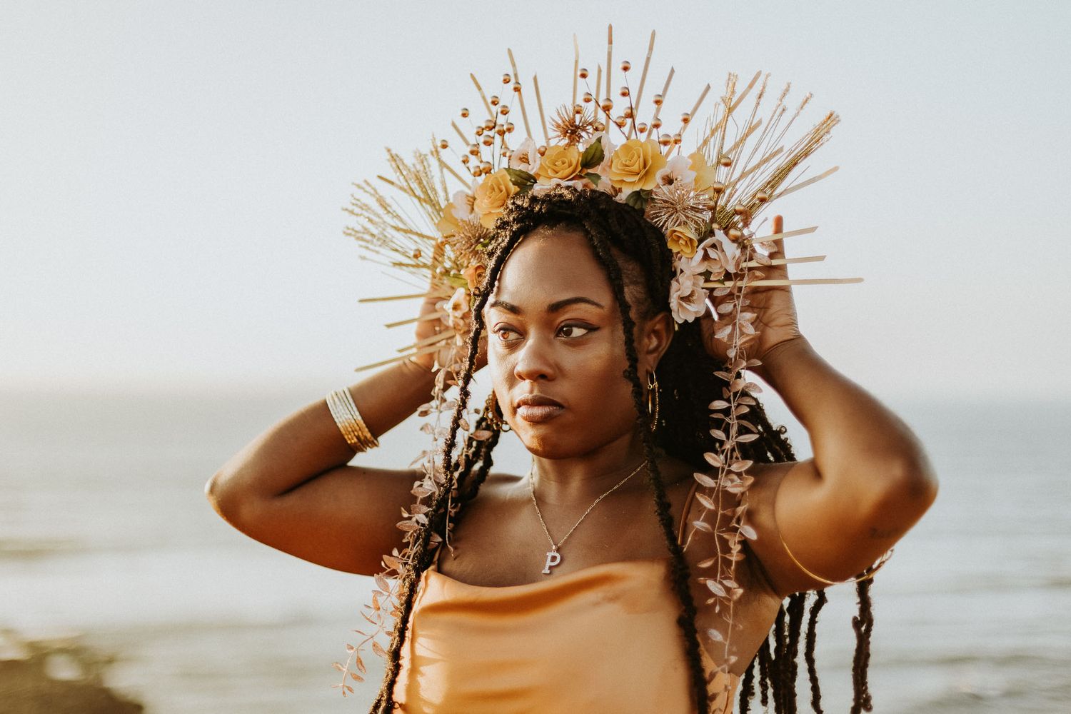 A woman wearing an ornate flower crown and gold dress poses at sunset in San Diego.