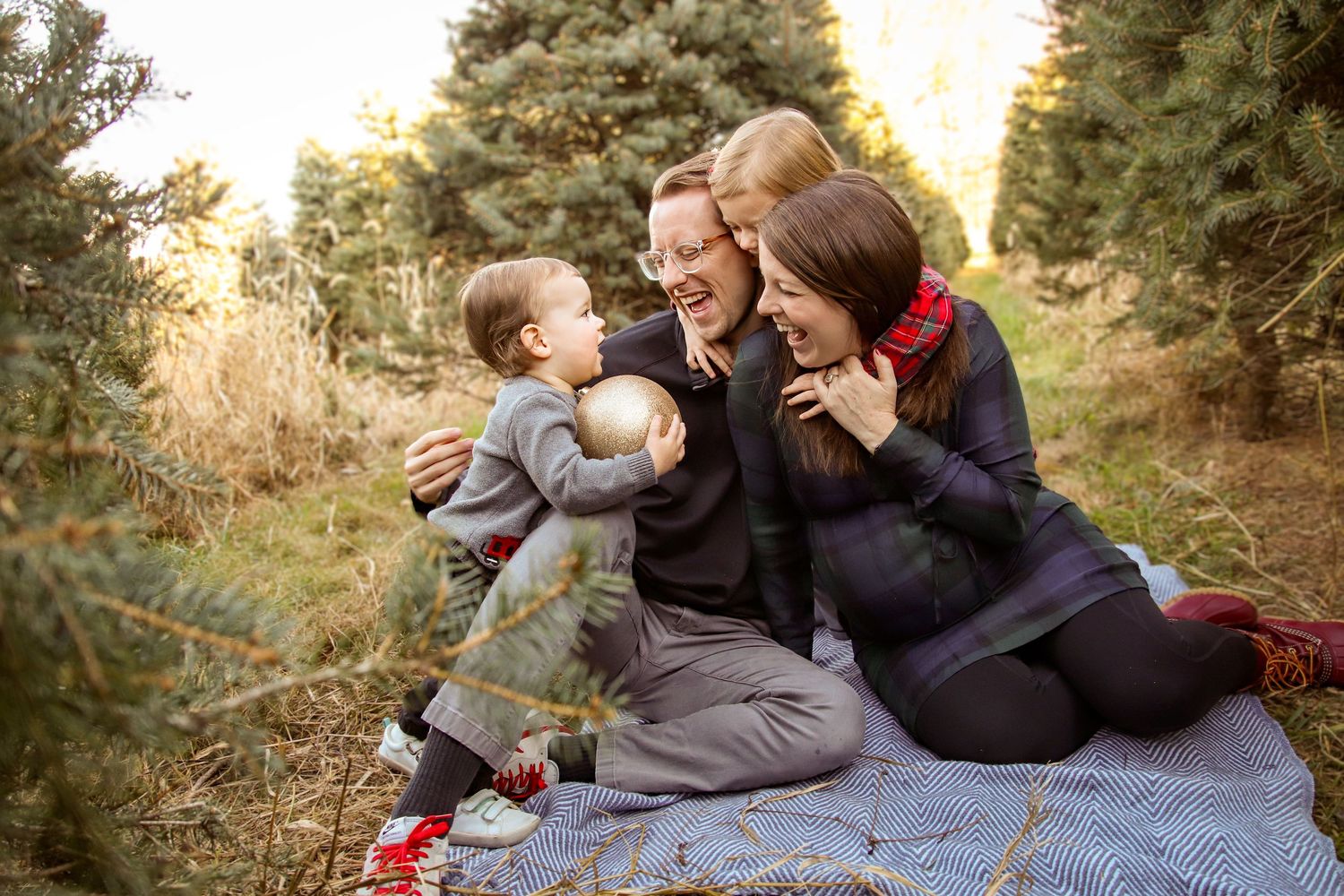 Family together on a blanket at a Christmas tree farm with a toddler holding a ornament during family photo session Glastonbury connecticut