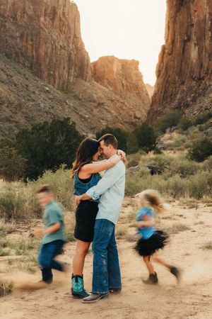 Couple embraces in desert canyon while two children run past in blur, capturing candid family moment in Southwest landscape.