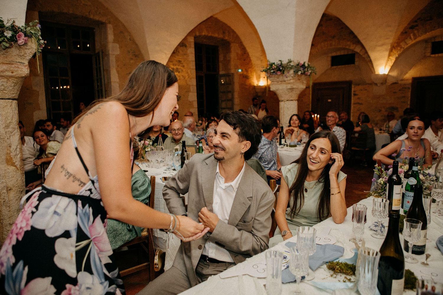 Guests socializing at an elegant wedding reception in a rustic stone venue with arched ceilings.