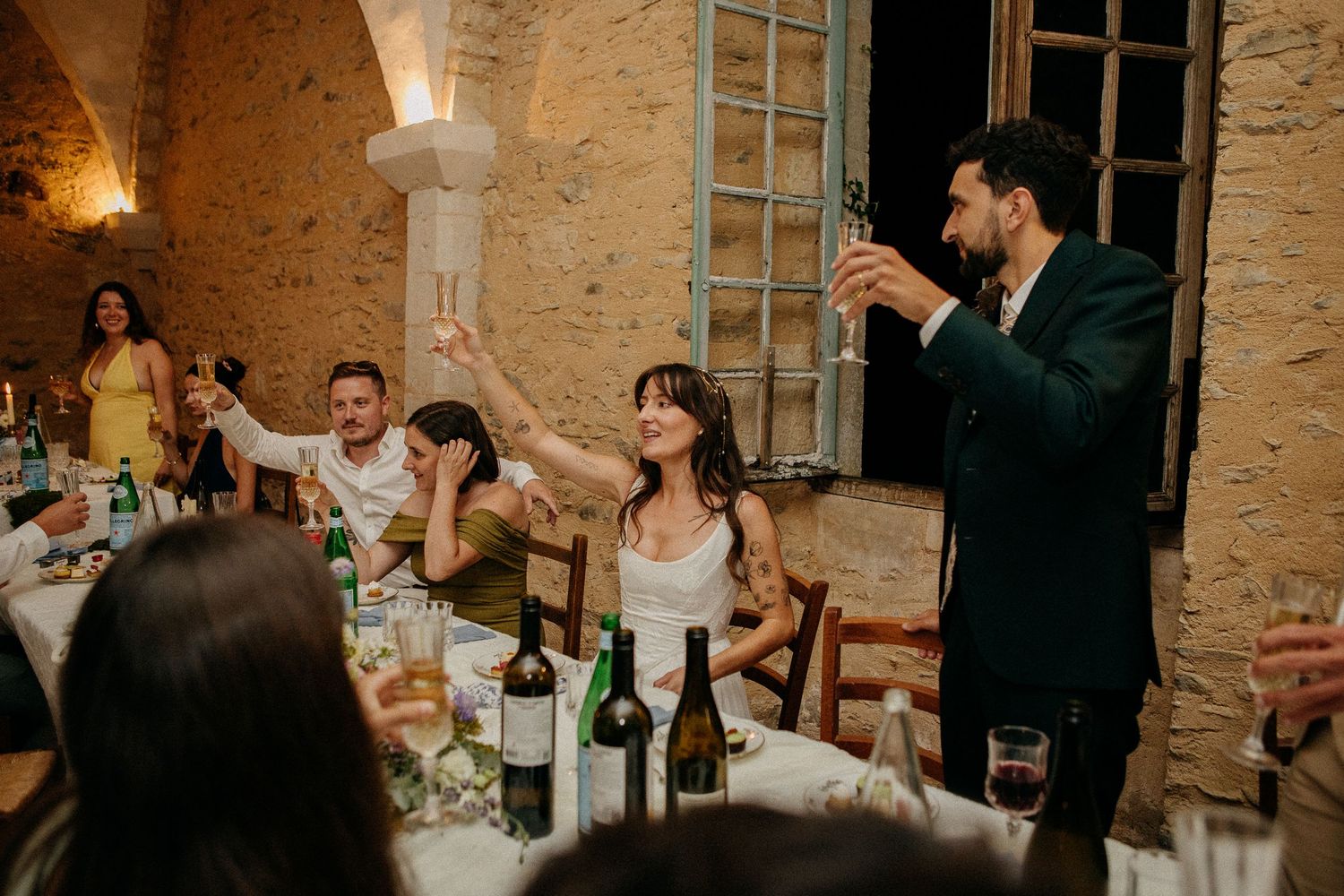 Wedding guests raising glasses in a toast at a rustic stone venue dinner reception.