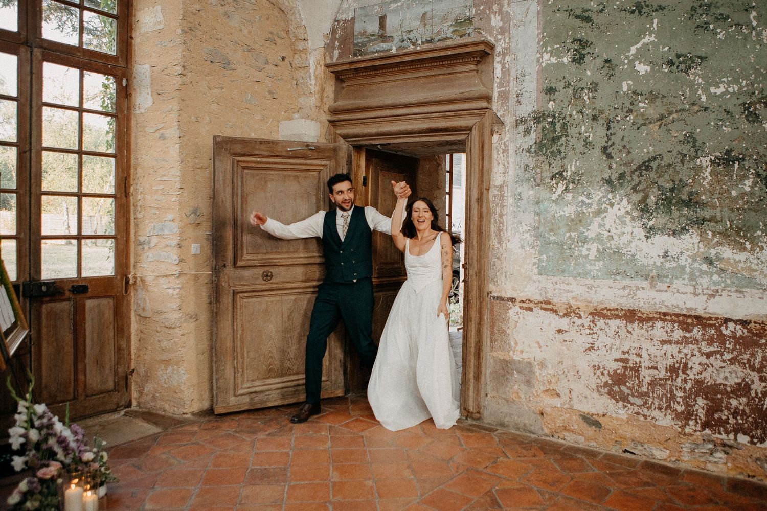Bride and groom smiling in doorway of rustic stone venue with terracotta floors on their wedding day.