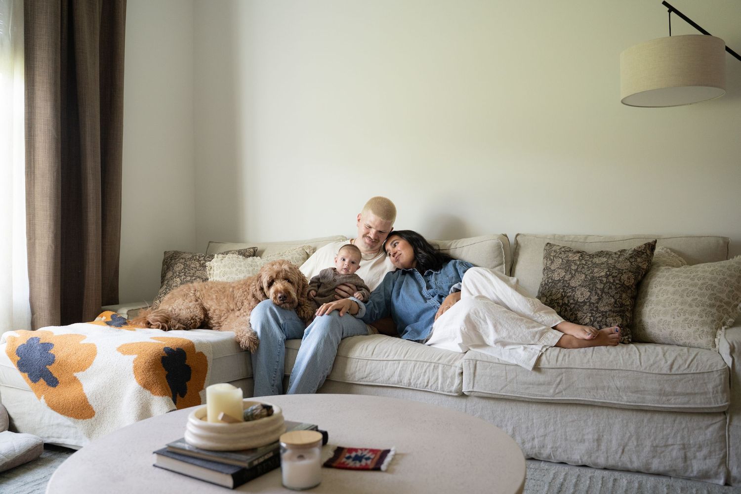 Family relaxing on a cozy sofa with their dog, reading a book together in a bright living room.