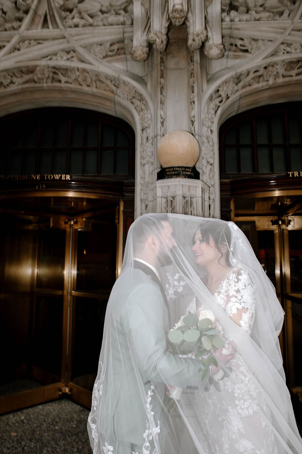 Bride and groom share a kiss under a flowing veil outside the Tribune Tower in Chicago.