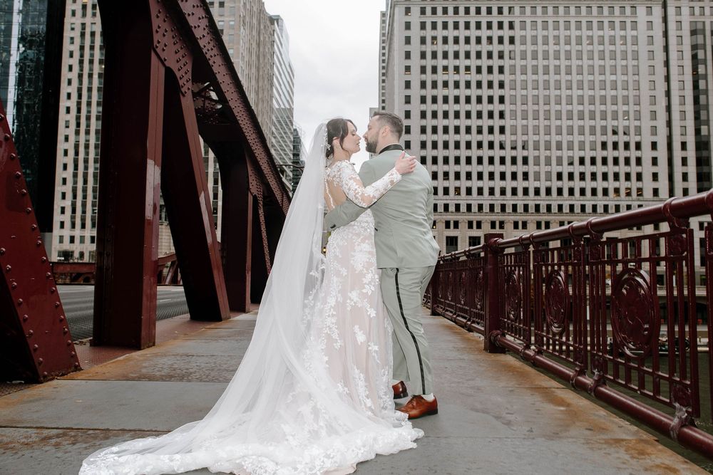 Bride and groom share a romantic moment on a red iron bridge with Chicago skyscrapers in the background.
